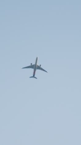 Vertical-Video-Of-Commercial-Jet-Flying-Overhead-Against-Blue-Sky